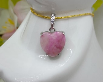 May include: A pink heart-shaped pendant with a silver setting and a silver chain. The pendant is on a white surface.