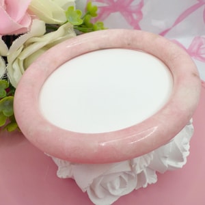 Peut inclure: Un bracelet jonc rose clair et lisse. Le bracelet circulaire semble être fait d'une pierre polie. Le fond comprend des accents floraux blancs et roses, et un présentoir blanc.
