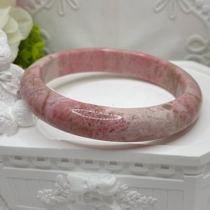 May include: A pink and white patterned bangle bracelet made of polished stone.