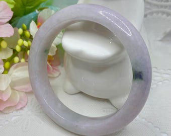 May include: A pale lavender jade bangle with green and white swirls. The bangle is smooth and polished.