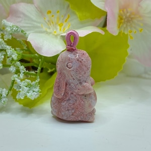 May include: A pink and white carved rabbit pendant with a pink loop for hanging. The rabbit is detailed with a lace-like pattern.