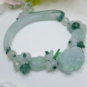 May include: A jade bracelet with a green and white floral design. The bracelet is made of jade beads and has a green string closure.
