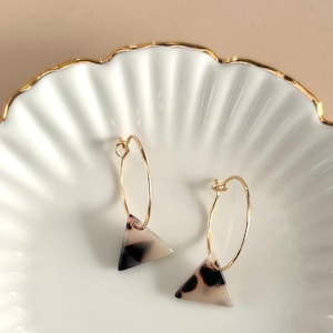 Può includere: Un paio di orecchini a cerchio dorati con un pendente a forma triangolare. Il pendente è fatto di tartaruga bianca e nera.