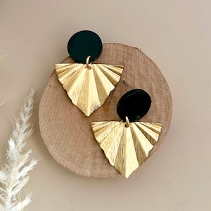 Könnte beinhalten: Ein Paar goldene Ohrringe mit schwarzen runden Akzenten. Die Ohrringe haben ein fächerförmiges Design mit einer strukturierten Oberfläche.