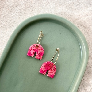 Può includere: Un paio di orecchini a cerchio a forma di arco con motivo rosa e bianco con cerchi dorati.