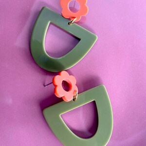 May include: A pair of green and orange earrings with a flower design. The earrings are made of acrylic and have a geometric shape.
