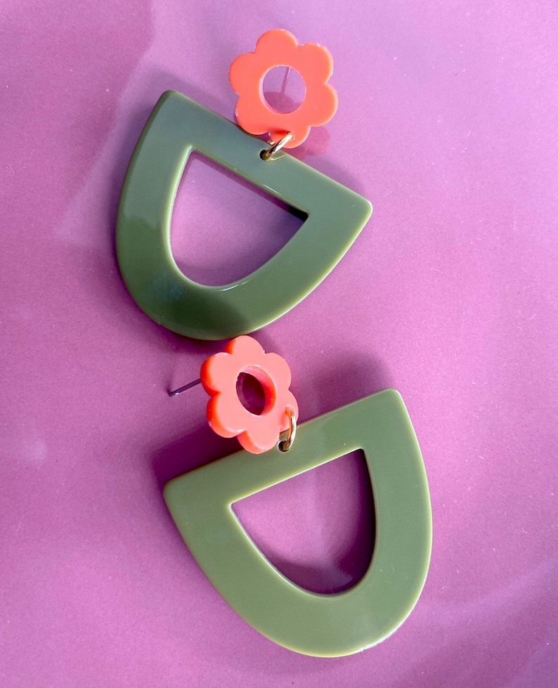May include: A pair of green and orange earrings with a flower design. The earrings are made of acrylic and have a geometric shape.