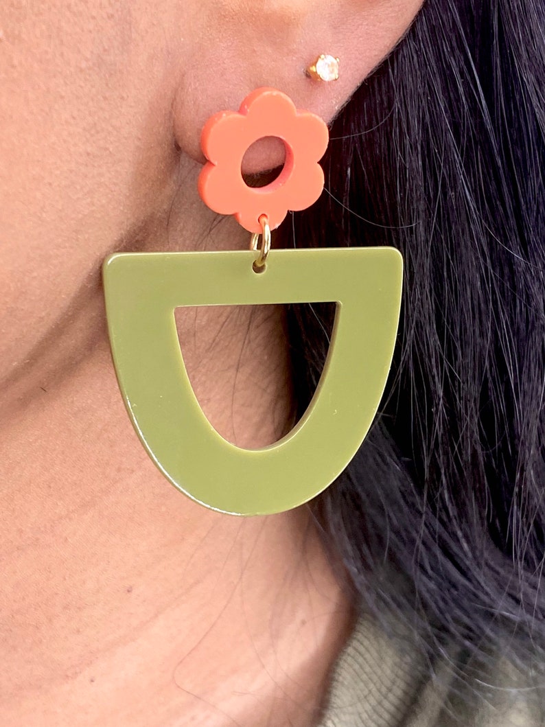 May include: A pair of earrings featuring a green geometric shape and a coral flower charm.
