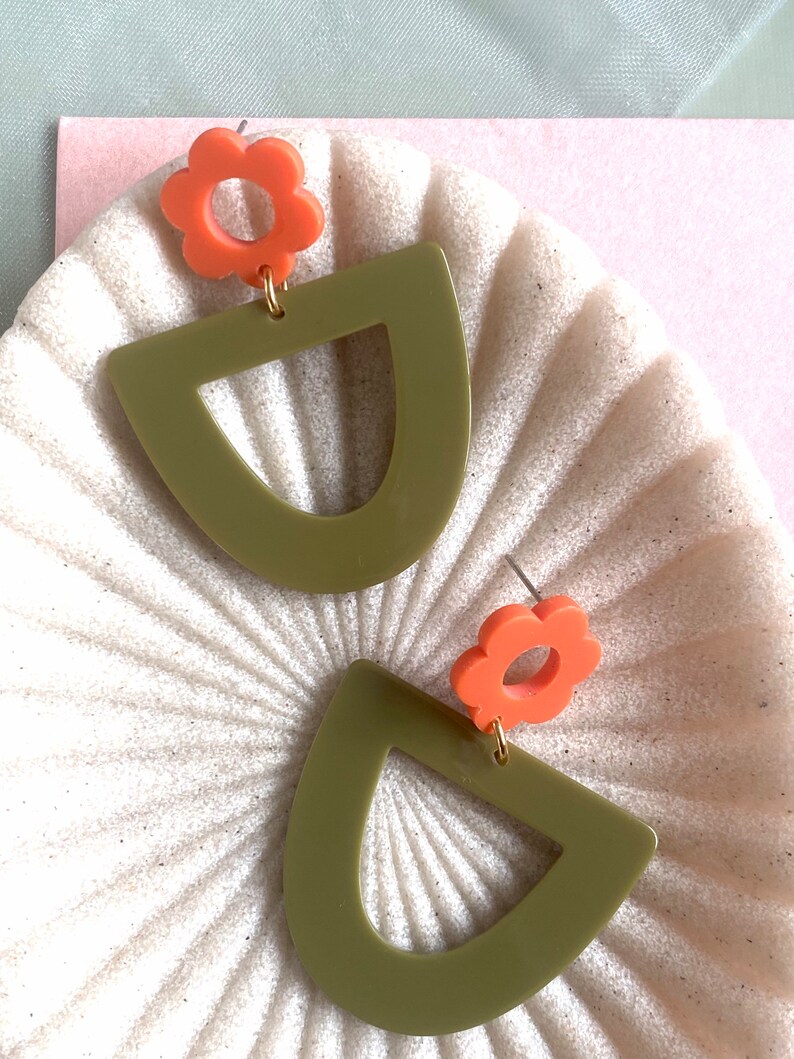 May include: A pair of earrings featuring a green geometric shape and a coral flower charm.
