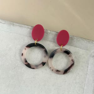 Può includere: Un paio di orecchini con una parte superiore ovale rossa e un grande cerchio con motivo bianco e nero.