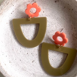 May include: A pair of earrings featuring a green geometric shape and a coral flower charm.
