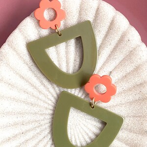 May include: A pair of green and coral earrings. The earrings are shaped like a half-circle with a smaller circle cut out of the centre. The top of each earring is adorned with a coral flower.