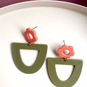 May include: A pair of earrings featuring a green geometric shape and a coral flower charm.