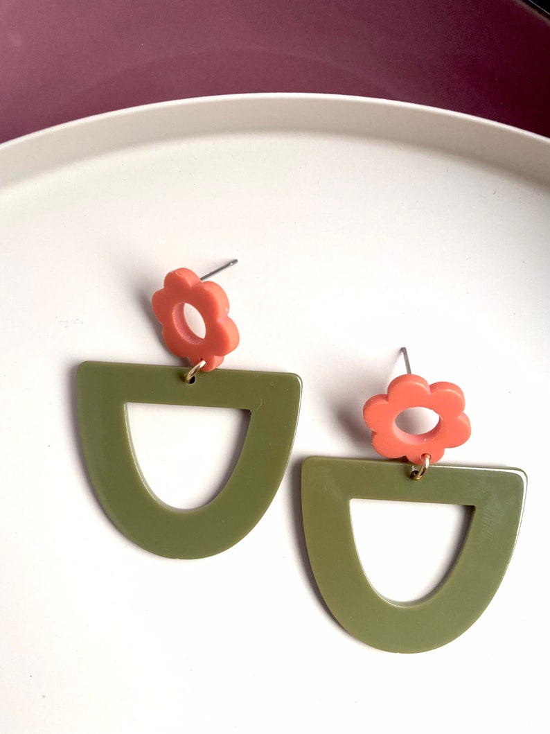 May include: A pair of earrings featuring a green geometric shape and a coral flower charm.
