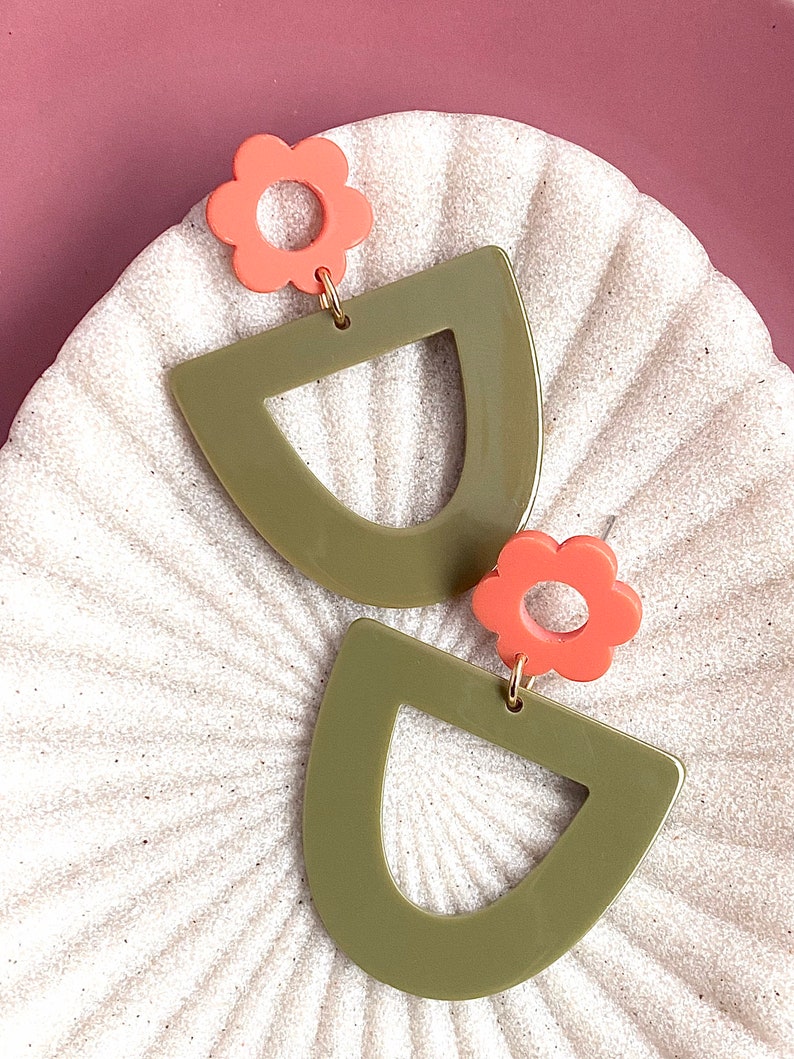 May include: A pair of green and coral earrings with a geometric shape and a flower design.