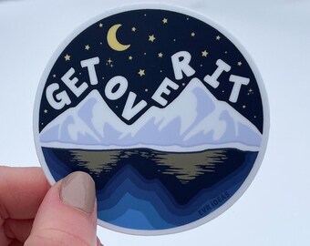 May include: A blue and white round sticker with the text "GET OVER IT" in white letters with a gold outline. The sticker features a crescent moon, stars, and mountains with a blue lake in the foreground.