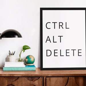 May include: A black framed print with the text "CTRL ALT DELETE" in white on a white background. The print is on a wooden desk with a black lamp, a small potted plant, a globe, and a stack of books.