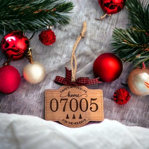 May include: Wooden Christmas ornament with a red and black plaid ribbon. The ornament is shaped like a house and has the text "There's no place like home 07005 for the holidays" on it.