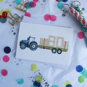 May include: A blue tractor pulling a trailer with bales of hay stacked to form the number 80. The card is a birthday card.
