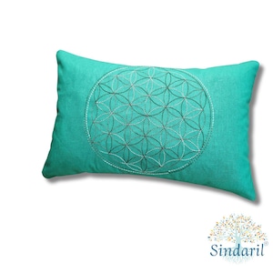Può includere: Cuscino rettangolare turchese con un ricamo dettagliato del Fiore della Vita al centro. Il ricamo è realizzato con filo bianco e grigio. Il cuscino è di colore turchese pieno. Il logo "Sindaril" si trova in basso a destra.