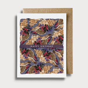 May include: A greeting card with a purple background and a pattern of seashells with pink and purple flowers. The text "Happy Birthday" is printed in black on a white ribbon.