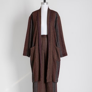 May include: A brown, striped two-piece outfit on a mannequin. The outfit comprises a long, open-front jacket with pockets and matching wide-leg trousers. The fabric features vertical stripes in shades of brown, grey, and a hint of purple.