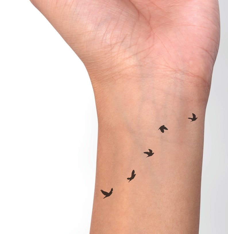 May include: A close-up of a person's wrist with a small tattoo of five black birds flying in a line.