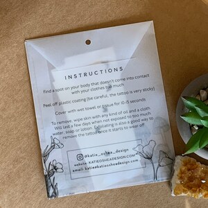 May include: Instructions for applying and removing a temporary tattoo. The instructions are printed on a white background with black text and a floral design. The text includes information about how to apply the tattoo, how long it will last, and how to remove it.