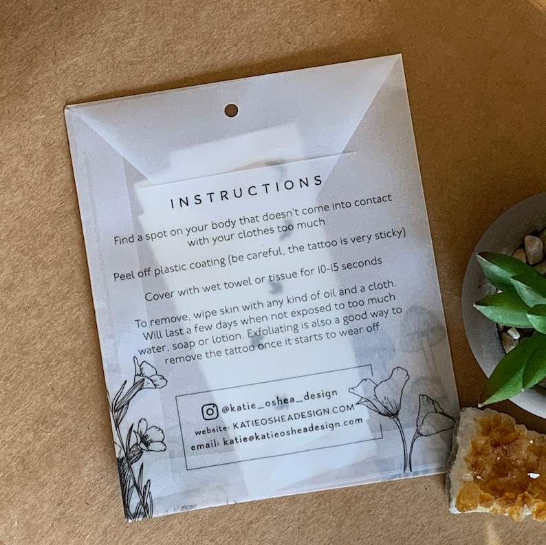 May include: Instructions for applying and removing a temporary tattoo. The instructions are printed on a white background with black text and a floral design. The text includes information about how to apply the tattoo, how long it will last, and how to remove it.