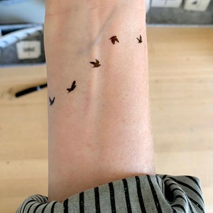 May include: A person's wrist with a small tattoo of five birds flying in a row.