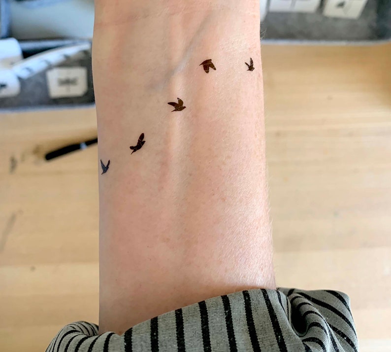May include: A person's wrist with a small tattoo of five birds flying in a row.