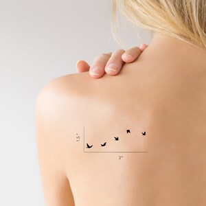 May include: A temporary tattoo of a flock of five black birds flying in a diagonal line. The tattoo measures 1.5 inches tall and 3 inches wide.