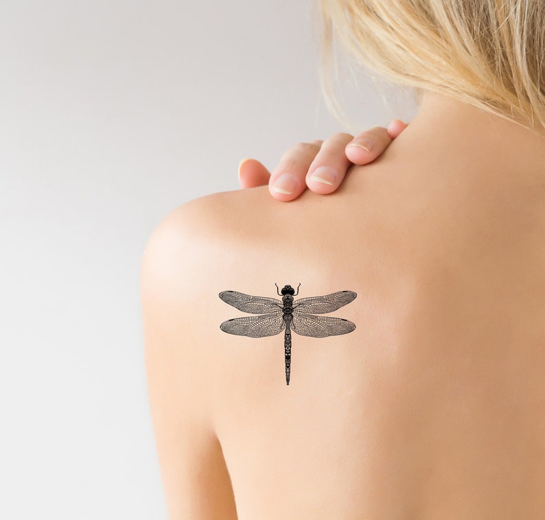 May include: A black and white dragonfly tattoo design on a person's shoulder.