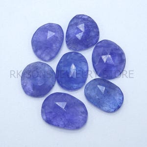 Peut inclure: Sept pierres précieuses bleu-violet en forme ovale et facettées. Les pierres précieuses ont une surface polie et sont disposées sur un fond blanc. Les pierres précieuses sont de tailles et de formes variables. Le texte "RK SONS JEWELRY STORE" est visible.