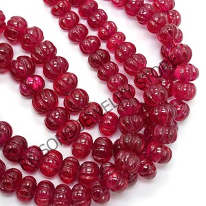May include: Strands of deep red, carved gemstone beads. The beads have a pumpkin-like shape with vertical grooves. The translucent beads are strung together, creating a rich, textured appearance. The beads are a vibrant, saturated color.