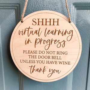 May include: A round wooden sign with the text "SHHH virtual learning in progress PLEASE DO NOT RING THE DOOR BELL UNLESS YOU HAVE WINE thank you" in a brown font. The sign is hanging from a natural twine rope.