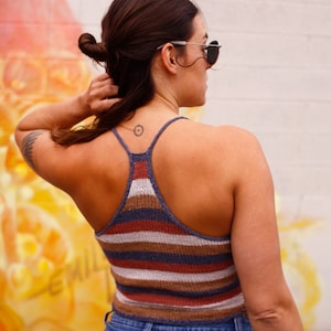 May include: A woman wearing a striped tank top and blue jeans. She has a small tattoo on her back.