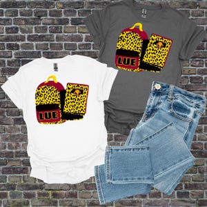 Op de afbeelding: Witte en grijze t-shirts met een rugzak- en notitieboekontwerp. De rugzak en het notitieboek hebben een geel luipaardpatroon met de letters "LUE" in rood. Lichtblauwe jeans zijn ook in de afbeelding.