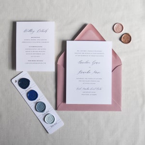 Puede incluir: Conjunto de invitaci&oacute;n de boda con una tarjeta de invitaci&oacute;n blanca dentro de un sobre rosa polvoriento. Incluye tambi&eacute;n una tarjeta de detalles, sellos de cera y una muestra de color de ceras azules. El texto de la invitaci&oacute;n est&aacute; en escritura elegante.