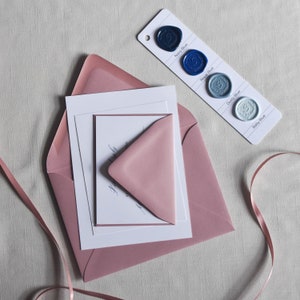 Puede incluir: Un juego de papeler&iacute;a con un sobre rosa rubor, un sobre m&aacute;s peque&ntilde;o a juego y tarjetas blancas. Una tarjeta de muestra de color muestra cuatro muestras de sellos de cera azules: Azul marino, Azul real, Azul polvoriento y Azul beb&eacute;. Tambi&eacute;n hay una cinta rosa.