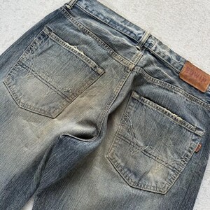 May include: Close-up of the back of faded blue denim jeans. The jeans have two back pockets with decorative stitching and a brown leather patch with the brand name "EDWIN". The denim has a worn, distressed look.