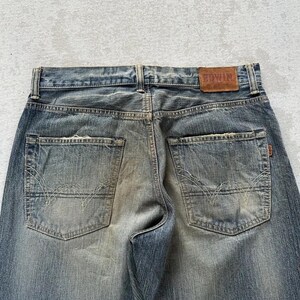 May include: Faded blue denim jeans with a classic five-pocket design. The back pockets feature a distinctive stitch pattern. A brown leather patch with the brand name "EDWIN" is visible at the waistband.