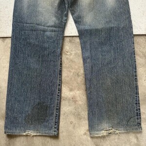 May include: Faded blue denim jeans with a worn appearance. The jeans show signs of wear and tear, with distressed areas near the bottom hems. The denim has a gradient effect, with lighter shades at the top and darker shades towards the bottom.