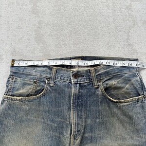 May include: Close-up of blue denim jeans with a tape measure across the waistband. The jeans show signs of wear and fading. The tape measure indicates a waist measurement of approximately 45.7 cm.