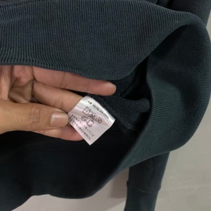 May include: Close-up of a dark teal sweatshirt with a ribbed cuff. A tag with Japanese text and laundry symbols is visible. The tag includes the product code KK-RL-KA-0526.