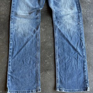 May include: Faded blue denim jeans with a straight leg cut. The jeans show wear and tear with visible fading and creases. The denim is a medium wash, with lighter areas on the thighs and knees.
