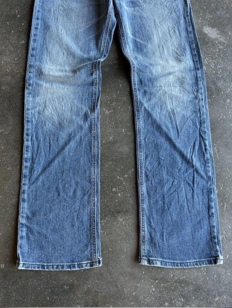 May include: Faded blue denim jeans with a straight leg cut. The jeans show wear and tear with visible fading and creases. The denim is a medium wash, with lighter areas on the thighs and knees.