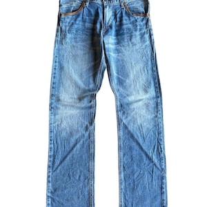 May include: Faded blue denim jeans with a classic five-pocket design. The jeans have a straight leg cut and feature brown leather accents around the front pockets. The denim has a worn, distressed look.