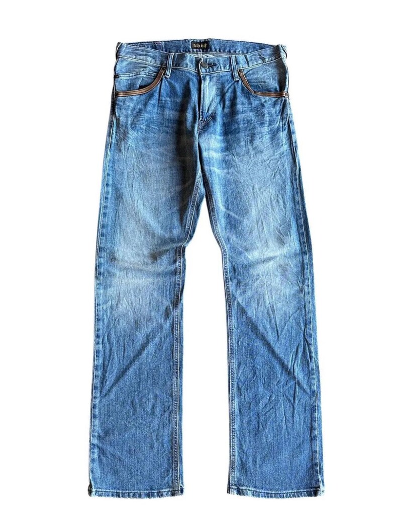 May include: Faded blue denim jeans with a classic five-pocket design. The jeans have a straight leg cut and feature brown leather accents around the front pockets. The denim has a worn, distressed look.