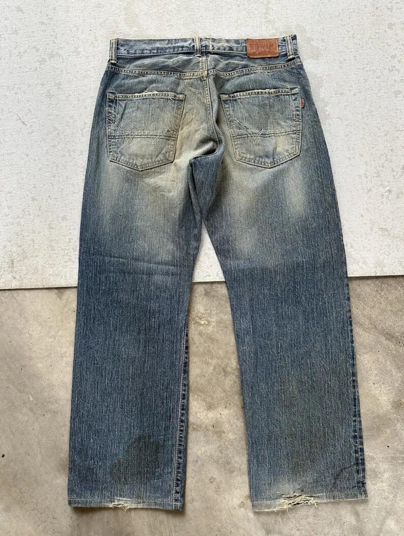 May include: Faded blue denim jeans with a distressed appearance. The jeans feature a classic five-pocket design, a leather patch, and a worn look. The jeans are a straight-leg style.